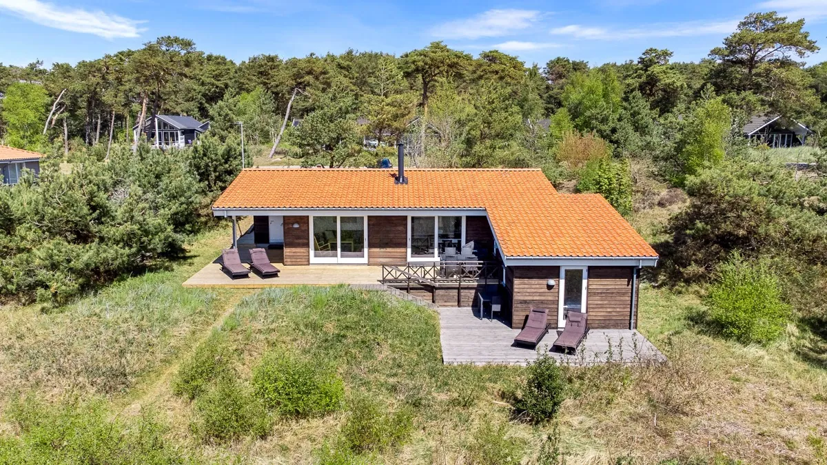 Træsommerhus med orange tegltag set fra luften